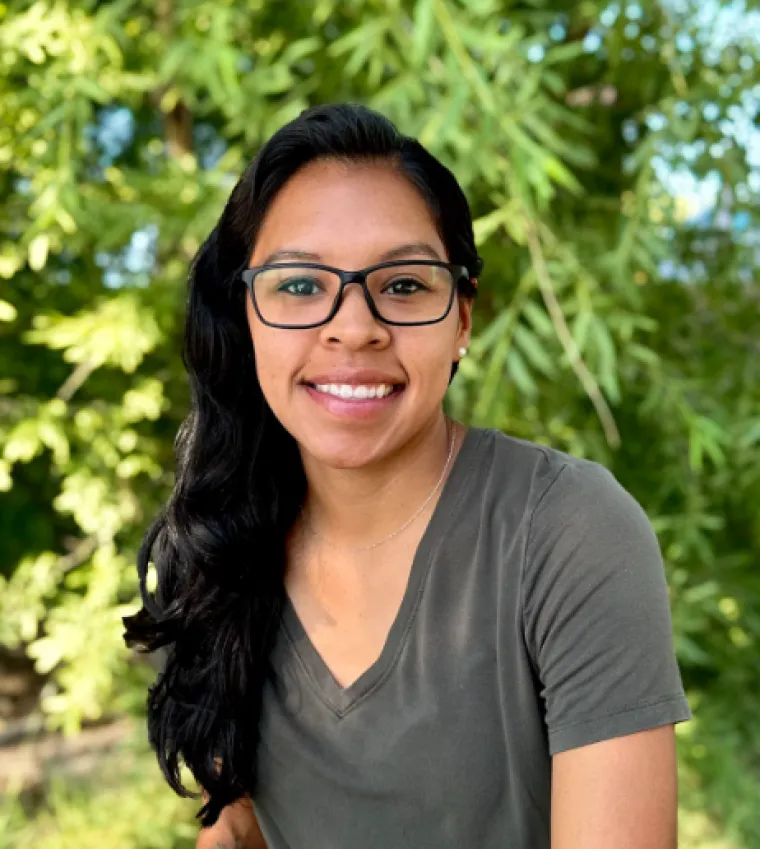 Headshot of Kelsey Montano, a hispanic woman with long dark hair, wearing glasses and a grey vneck tshirt.