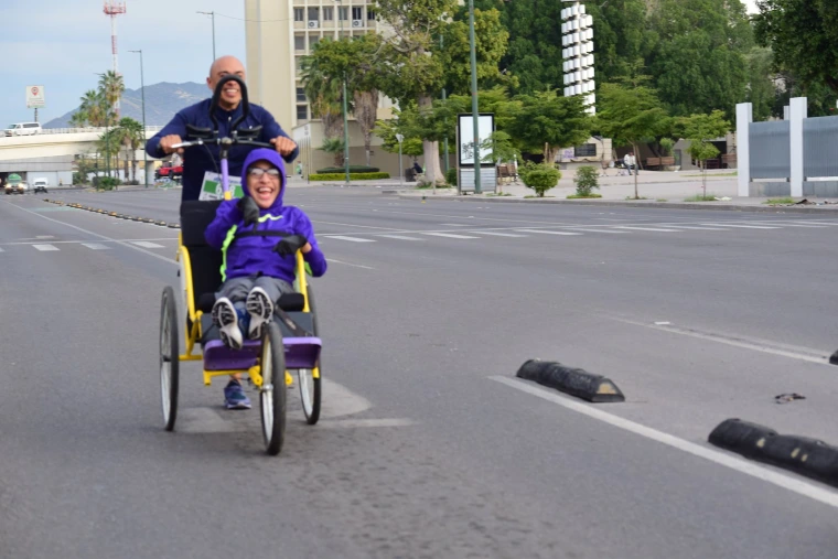 A smiling racer in a wheelchair is helped along the track by their supporter