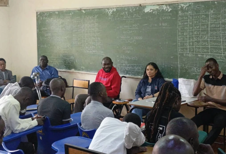 Denis and Jacy in front of a blackboard, speaking with students in a classroom. 