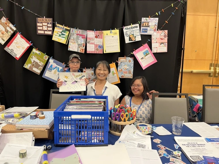 A young conference attendee, next to Yumi and Paavi, shows off the scrapbook page they created