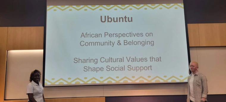 Mai and Kelvin standing on either side of a projector screen showing the title slide of their presentation