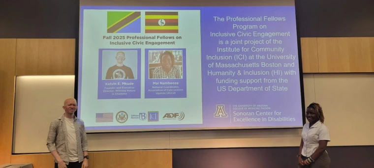 Kelvin and Mai standing on either side of a projector screen showing their bios and info about the Professional Fellows program