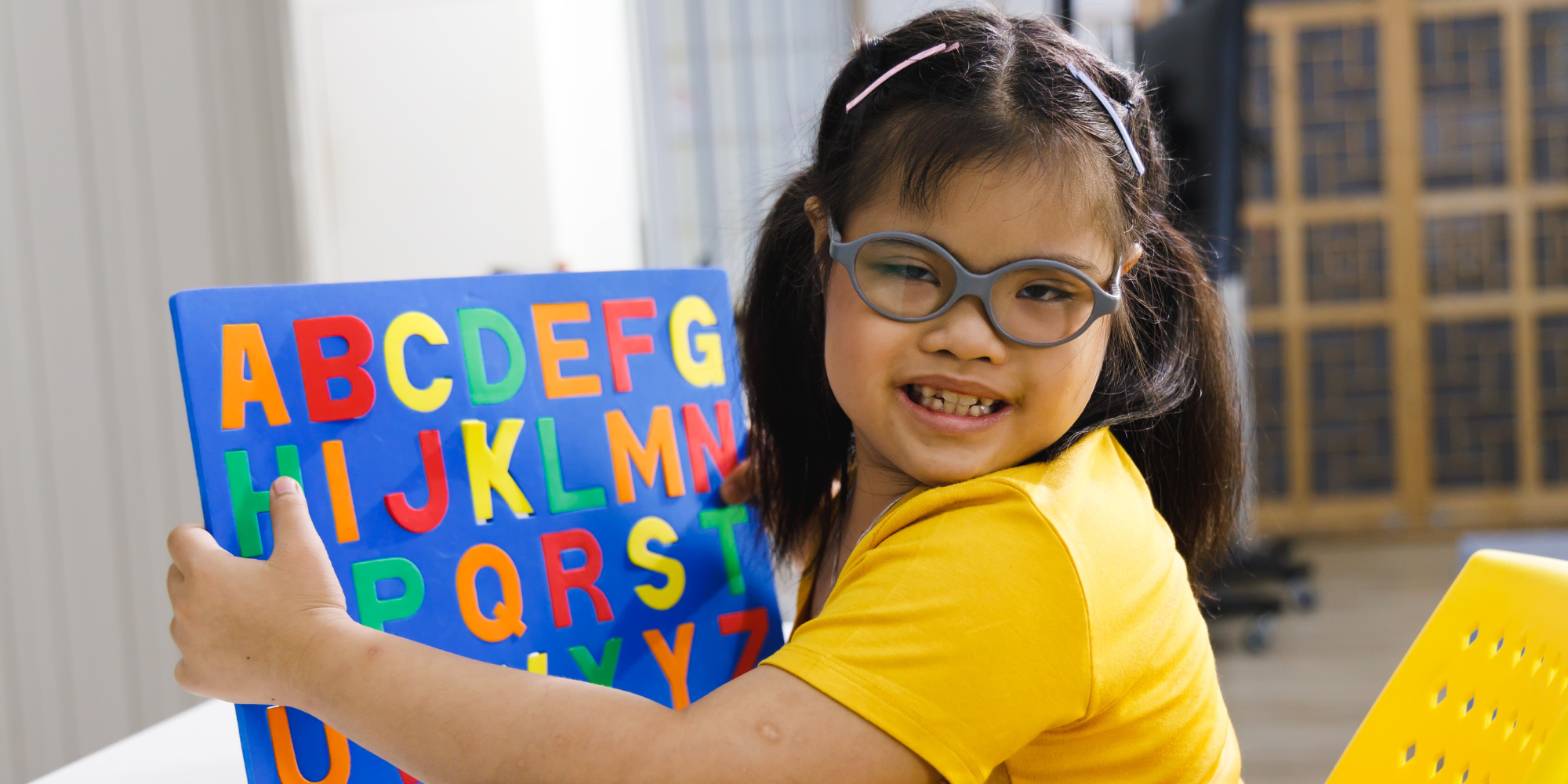 A young brunette girl with Down Syndrome holding up a letter board