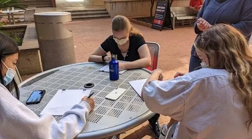 Three people sitting at a table outside and drawing