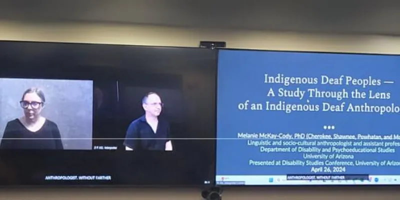 Two people in Zoom windows on a large presentation screen next to a powerpoint slide saying, "Indigenous Deaf Peoples..."