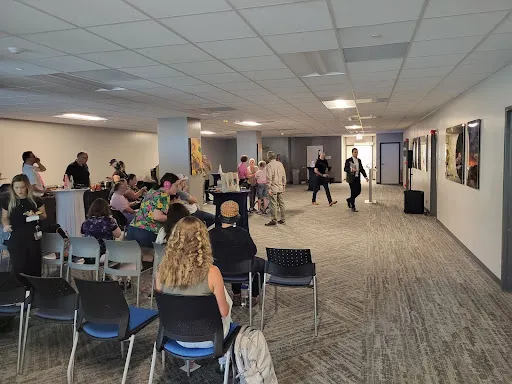 A wide view of the social hall. Attendees converse and enjoy refreshments. A harpist is playing in the background.