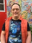 Image of Scott, a man with short brown hair wearing a black T-shirt and red puffer vest, smiling in front of a mosaic mural.