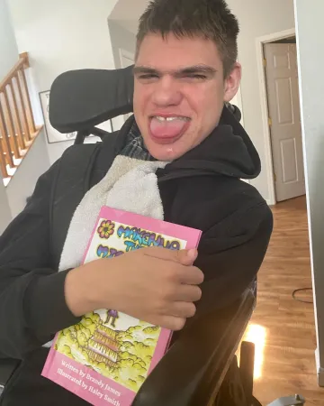 A Man smiling and holding Makenna the Mighty book