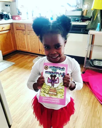 A little girl smiling and holding Makenna the Mighty book