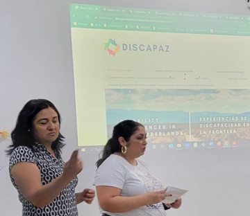 Sign language interpreter (left) and Celina Urquidez (right) standing in front of a projector displaying the DISCAPAZ website homepage, giving a presentation