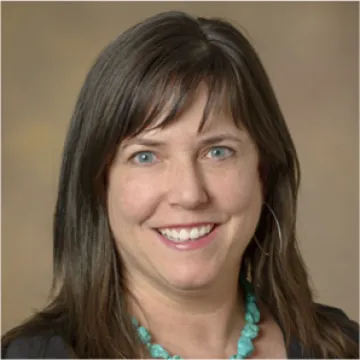 Julie Armin, PhD., a white woman with long brown hair wearing a turquoise necklace and brown top