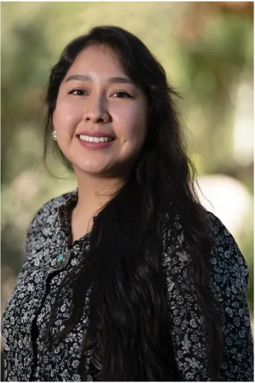 Woman with long dark hair wearing a black and white floral blouse