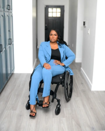 Lizzy O, a Black woman, wearing a light blue suit and sitting in a wheelchair