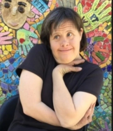 Photo of Carol, a woman with short brown hair wearing a black shirt and posing in front of a colorful mosaic mural.