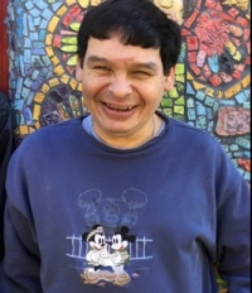 Image of Chris, a man with short black hair and wearing a blue shirt, smiling in front of a colorful mosaic mural.