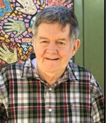 Ricky wearing a plaid shirt and is standing in front of a mural