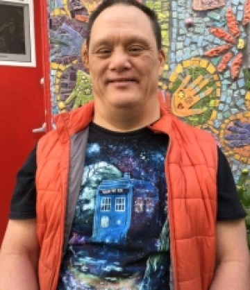 Image of Scott, a man with short brown hair wearing a black T-shirt and  red puffer vest, smiling in front of a mosaic mural.