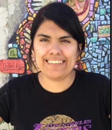 Image of Vanessa, a woman with dark brown hair and brown eyes, wearing a black shirt and smiling in front of a mosaic mural.
