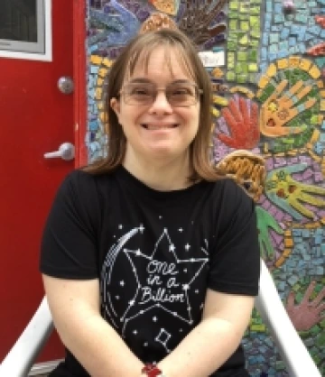 Vicky is wearing a black shirt and glasses and is smiling at the camera