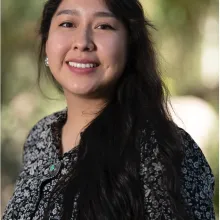 Woman with long dark hair wearing a black and white floral blouse