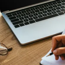 Hands taking notes in front of a laptop.