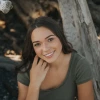 Alexia Tawrel, a young woman sitting outside in a wooded area, looking up at the camera and smiling