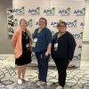 Jessica Winchester (left) and Rosa Rojas Franco (right) pose in front of a banner with the logo of the APSE One Voice Conference. 