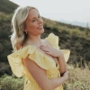 Lauren Elizabeth Mitchell, wearing a yellow dress and standing in a field, smiling