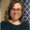 Jennifer Haggerty, a woman with long brown hair, wearing glasses and a black top, smiling