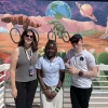 Mai Nambooze and Kelvin Mkude standing with Loretta Alvarez in front of a Sonoran Desert-themed mural