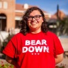 Lexicon Espinoza, a UA student with shoulder-length brown hair and glasses, wearing a Bear Down shirt, standing outside on the UA campus