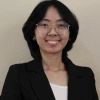 Nadine Chau, a young person with shoulder length black hair and glasses, wearing a white top and black blazer, smiling